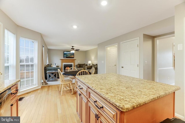 kitchen featuring a lit fireplace, light stone countertops, dishwasher, light wood finished floors, and brown cabinetry