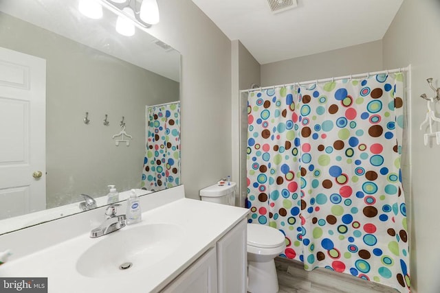 bathroom with curtained shower, toilet, wood finished floors, vanity, and visible vents