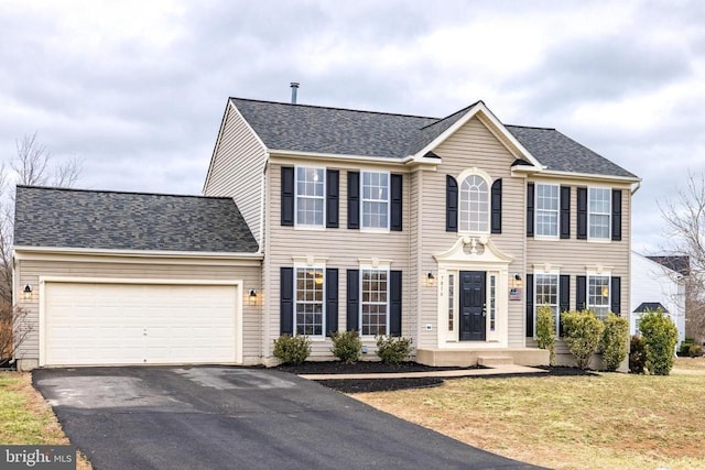 colonial home with aphalt driveway, roof with shingles, an attached garage, and a front lawn