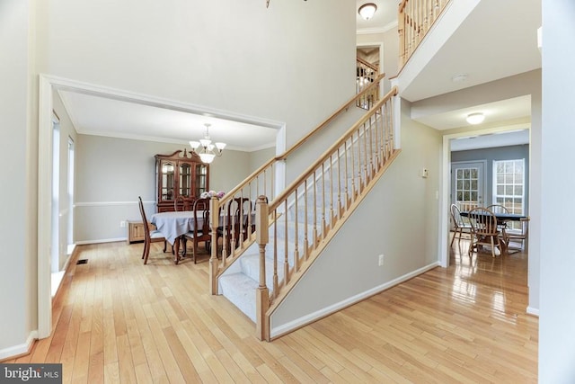 staircase with a notable chandelier, a towering ceiling, hardwood / wood-style flooring, and crown molding