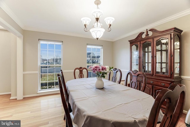 dining space featuring light wood-type flooring, crown molding, baseboards, and an inviting chandelier