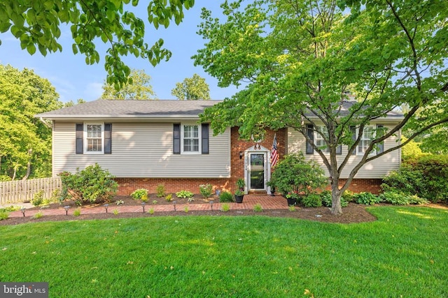 raised ranch featuring brick siding, a front yard, and fence