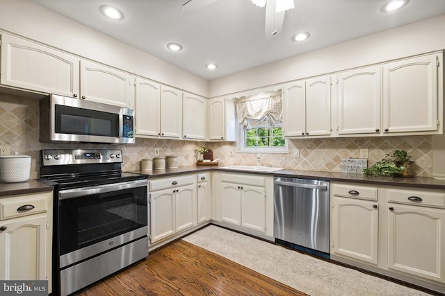 kitchen featuring a sink, dark countertops, dark wood finished floors, appliances with stainless steel finishes, and decorative backsplash