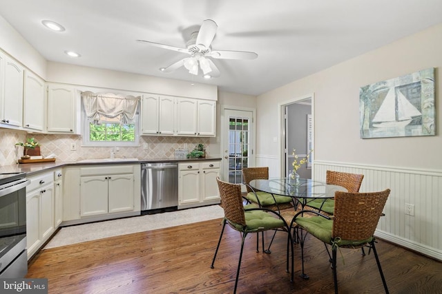 kitchen with a sink, a wainscoted wall, appliances with stainless steel finishes, and white cabinetry