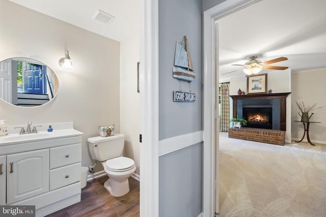 bathroom with a brick fireplace, ceiling fan, baseboards, toilet, and vanity