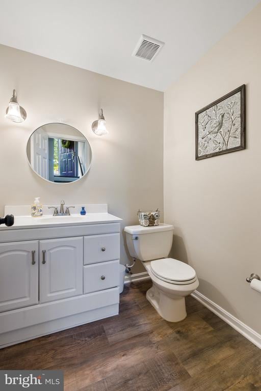 bathroom featuring visible vents, baseboards, toilet, wood finished floors, and vanity