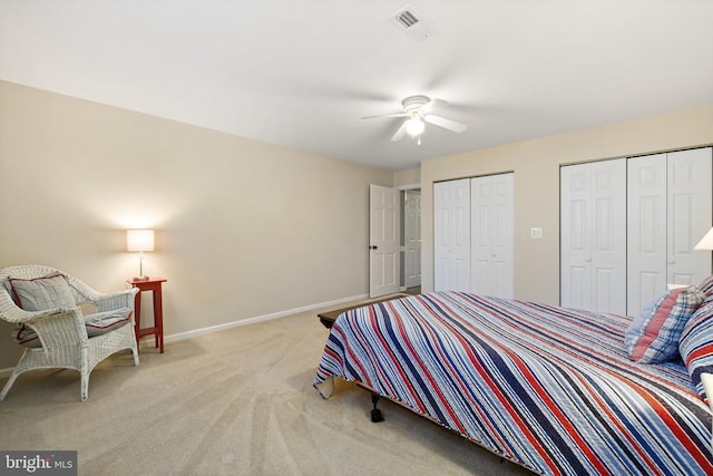 bedroom featuring visible vents, baseboards, ceiling fan, light colored carpet, and two closets