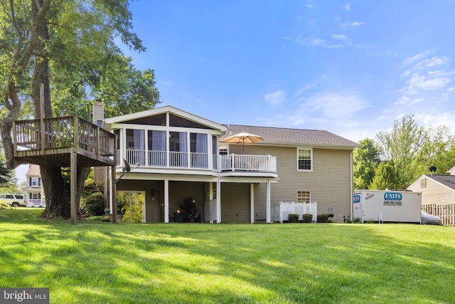 rear view of property with a yard, a deck, a chimney, and a sunroom