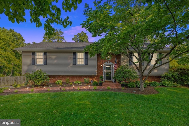 split foyer home featuring brick siding, a front yard, and fence