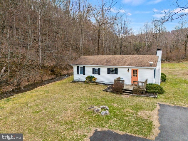 view of front of property featuring roof with shingles, a chimney, a wooded view, a front lawn, and a wooden deck