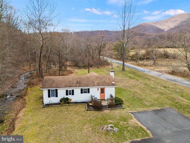 view of front facade with a deck with mountain view, a forest view, and a front yard