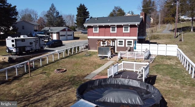 rear view of property with a lawn, a deck, a detached garage, a fenced backyard, and an outdoor fire pit