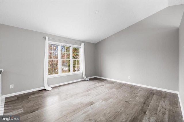 empty room with vaulted ceiling, wood finished floors, and baseboards