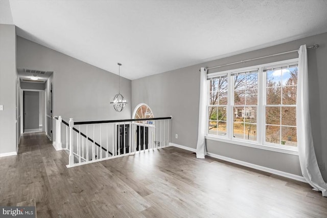 spare room with visible vents, baseboards, a chandelier, vaulted ceiling, and wood finished floors