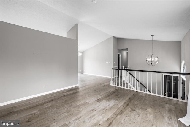 unfurnished room with baseboards, lofted ceiling, an inviting chandelier, and wood finished floors