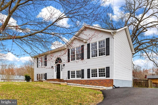 raised ranch featuring brick siding, driveway, a front yard, and fence