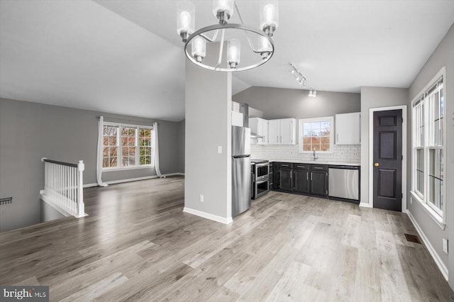 kitchen featuring light wood finished floors, stainless steel appliances, white cabinetry, a notable chandelier, and tasteful backsplash