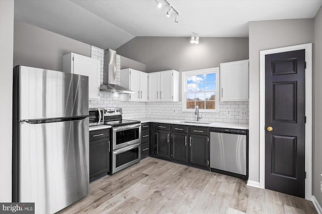 kitchen with light countertops, lofted ceiling, stainless steel appliances, wall chimney exhaust hood, and a sink