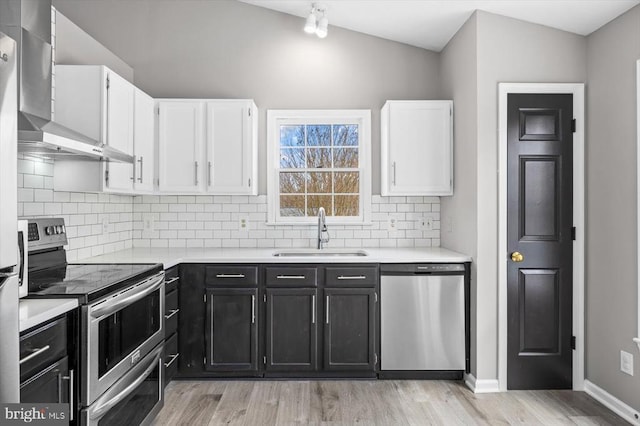 kitchen featuring a sink, appliances with stainless steel finishes, white cabinetry, wall chimney exhaust hood, and dark cabinets