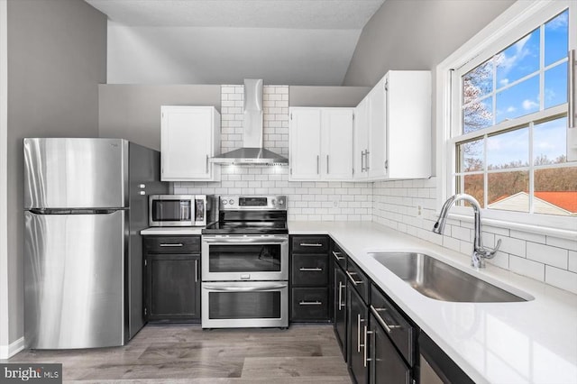 kitchen featuring a sink, stainless steel appliances, white cabinets, wall chimney range hood, and dark cabinets