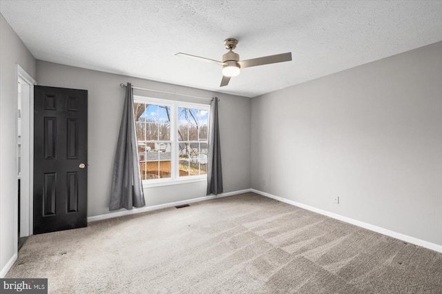 carpeted spare room with visible vents, baseboards, and ceiling fan