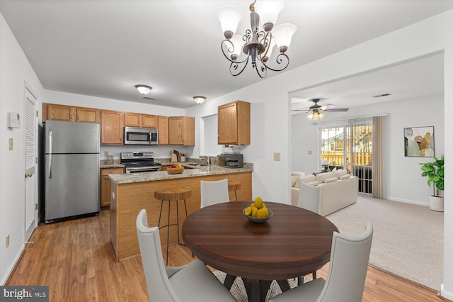 dining room featuring ceiling fan with notable chandelier, light colored carpet, light wood-style flooring, and baseboards