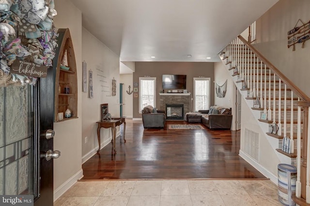 entryway with stairway, wood finished floors, visible vents, baseboards, and a stone fireplace