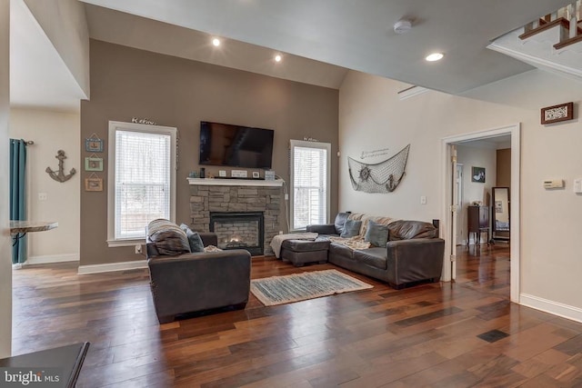 living area with baseboards, a stone fireplace, recessed lighting, a towering ceiling, and wood finished floors