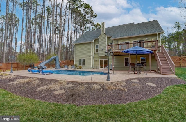 rear view of house with a fenced backyard, a deck, a chimney, and a patio area