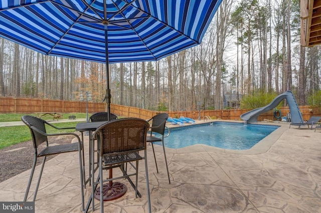 view of pool featuring a patio, a fenced in pool, a water slide, outdoor dining area, and a fenced backyard