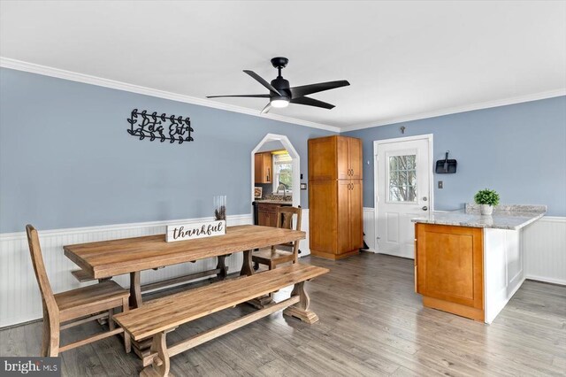 dining area featuring ceiling fan, ornamental molding, wainscoting, and light wood finished floors
