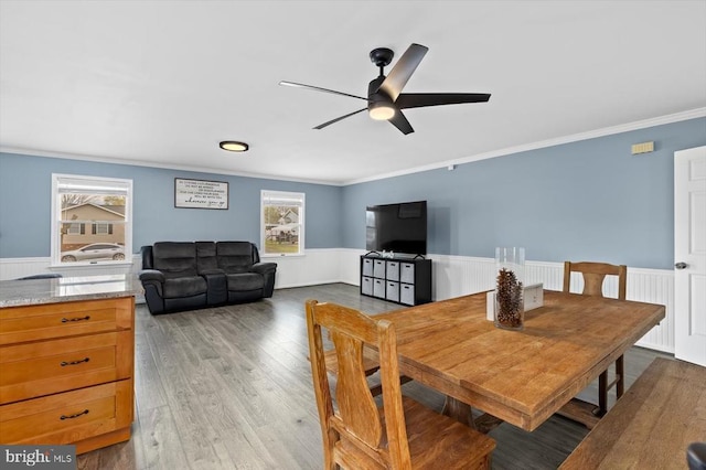 dining area with a ceiling fan, a wainscoted wall, ornamental molding, and wood finished floors