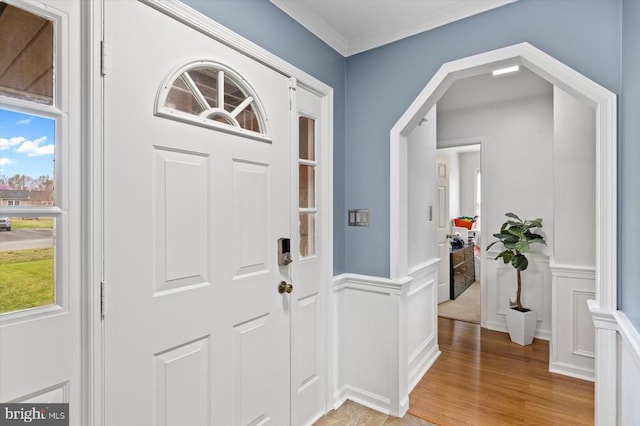 foyer entrance featuring a decorative wall, crown molding, light wood-style floors, and wainscoting