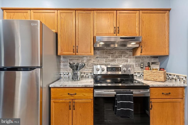 kitchen with light stone counters, stainless steel appliances, under cabinet range hood, and decorative backsplash