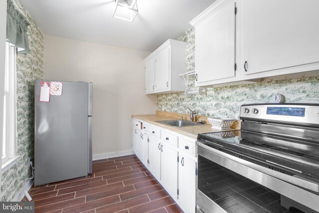 kitchen featuring light countertops, a sink, white cabinetry, stainless steel appliances, and wood tiled floor