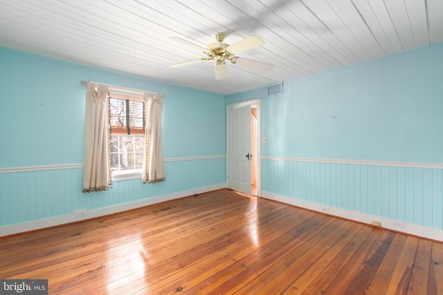 unfurnished room with hardwood / wood-style floors, visible vents, ceiling fan, and wainscoting