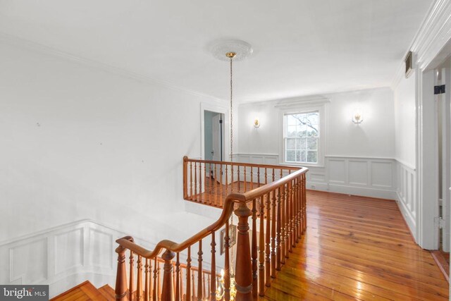 hall with an upstairs landing, visible vents, a decorative wall, crown molding, and hardwood / wood-style floors