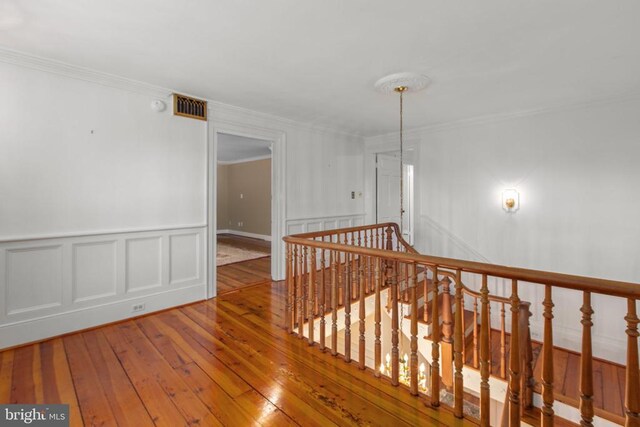 hall featuring an upstairs landing, a decorative wall, visible vents, ornamental molding, and hardwood / wood-style floors