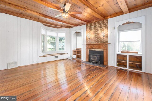 unfurnished living room featuring visible vents, beam ceiling, a wood stove, wood ceiling, and wood-type flooring