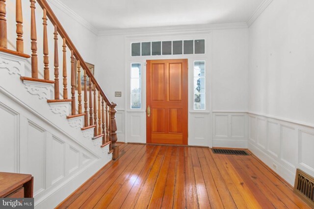 entryway featuring crown molding, stairway, light wood-style flooring, visible vents, and a decorative wall