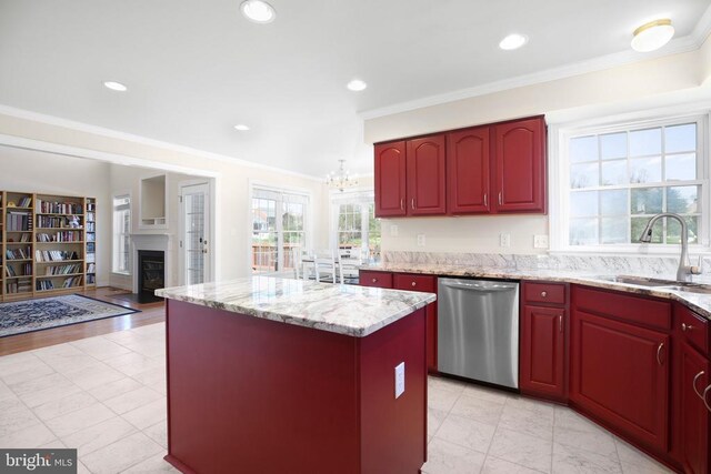 kitchen featuring stainless steel dishwasher, crown molding, a sink, a kitchen island, and a glass covered fireplace