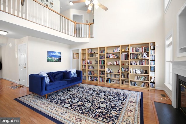 living room with a high ceiling, ceiling fan, a glass covered fireplace, baseboards, and wood finished floors