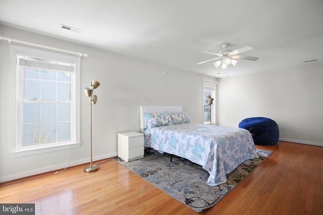 bedroom featuring wood-type flooring, visible vents, ceiling fan, and baseboards
