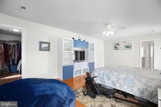 bedroom with a spacious closet, wood finished floors, a closet, ceiling fan, and visible vents