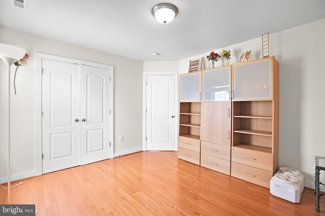 unfurnished bedroom featuring baseboards, visible vents, a closet, and light wood finished floors