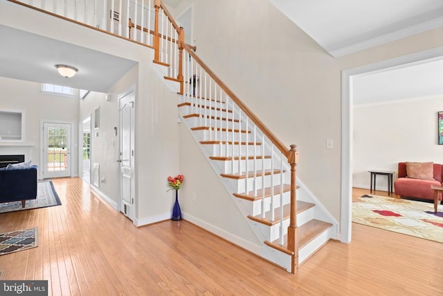 stairway featuring ornamental molding, hardwood / wood-style floors, baseboards, and a fireplace
