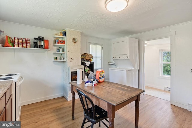 dining room featuring baseboards, stacked washer and clothes dryer, light wood finished floors, and a baseboard heating unit