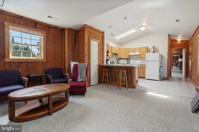 living area featuring visible vents, vaulted ceiling with skylight, and wooden walls