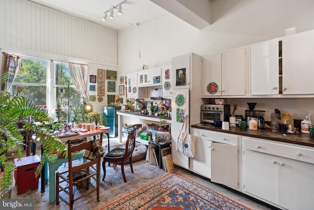 kitchen with white cabinetry, dark countertops, track lighting, and a towering ceiling