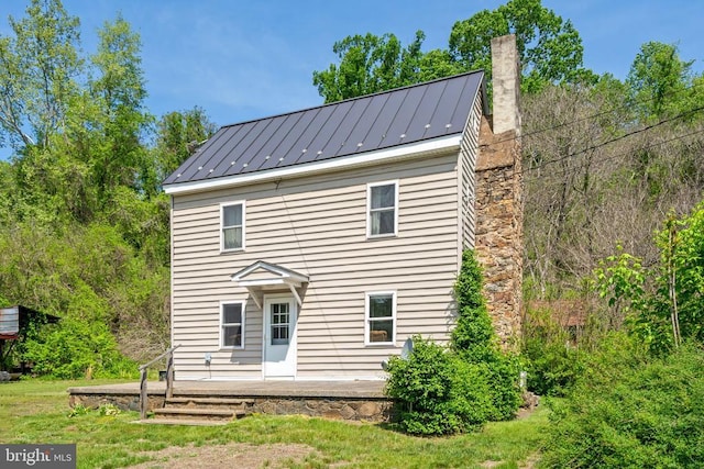 rear view of house with a standing seam roof, a chimney, and metal roof
